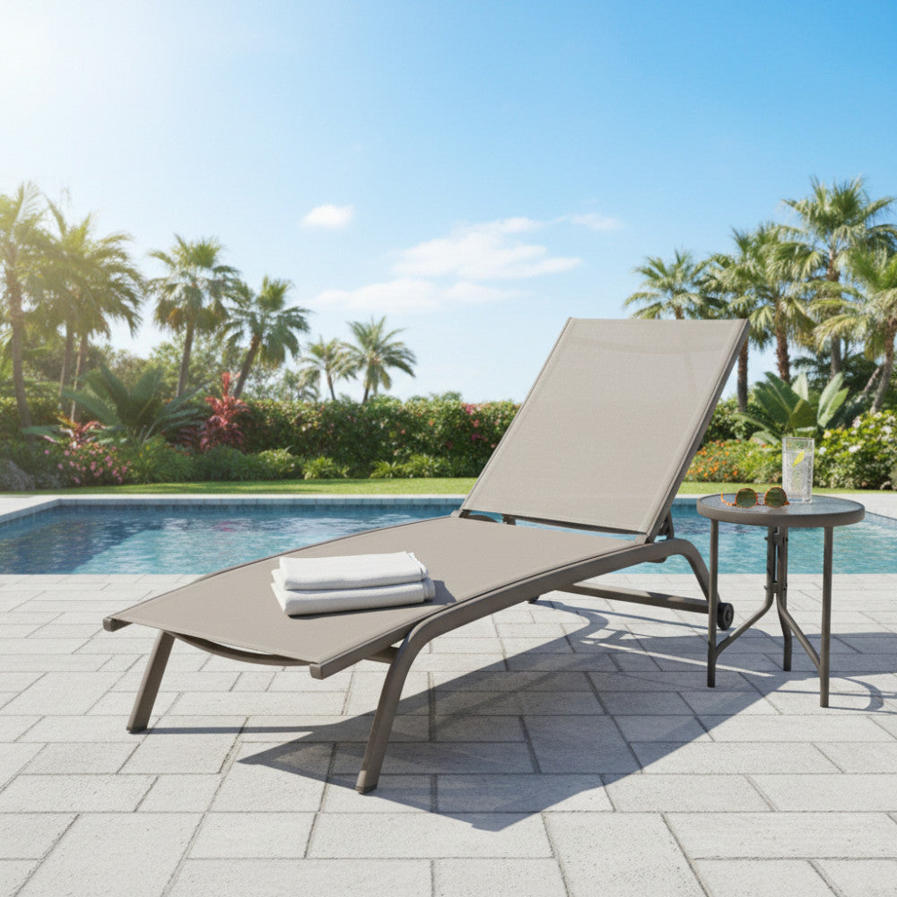 Lettino di design Itaca su pavimentazione in pietra vicino a una piscina circondato da palme tropicali e vegetazione lussureggiante.
