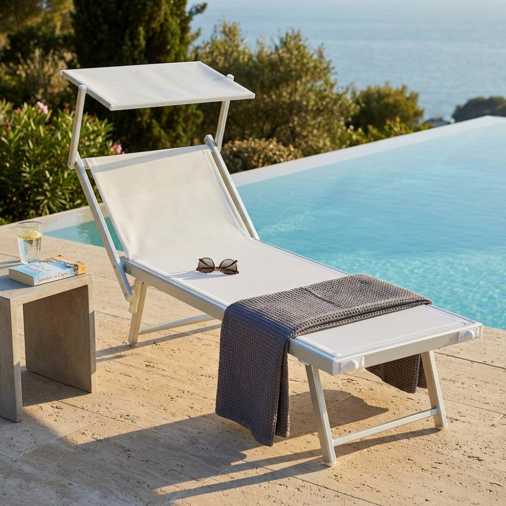 Lettino prendisole Jesolo in alluminio bianco con parasole regolabile, allestito a bordo piscina con telo grigio e occhiali da sole.