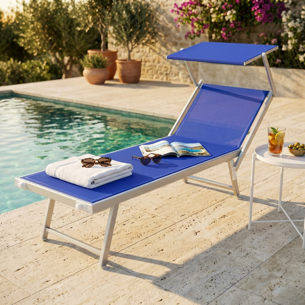 Lettino prendisole Jesolo in alluminio con seduta blu, posizionato a bordo piscina accanto a un tavolino bianco.