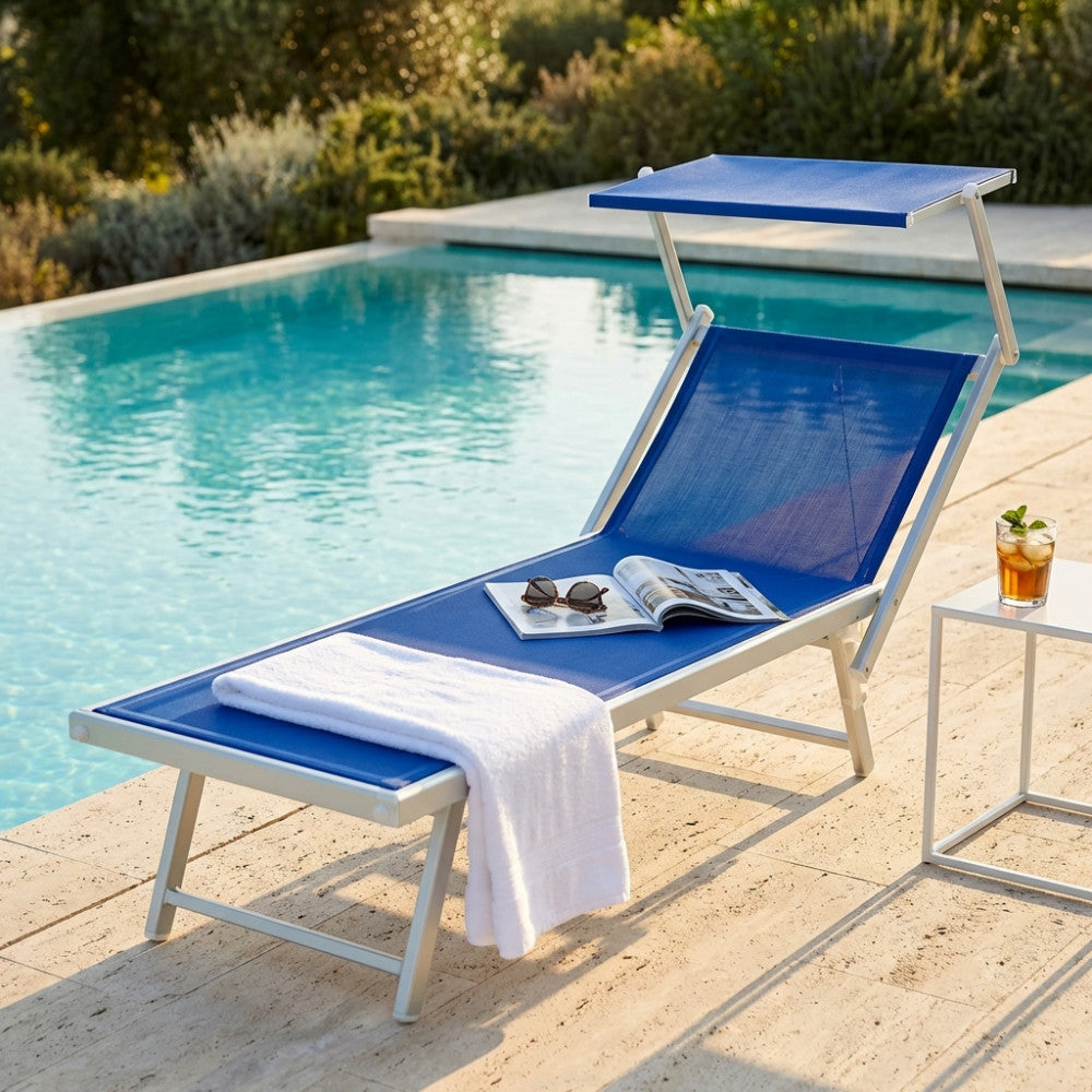 Dettaglio del lettino prendisole Jesolo blu con parasole regolabile, ambientato in un giardino lussuoso vicino all'acqua.