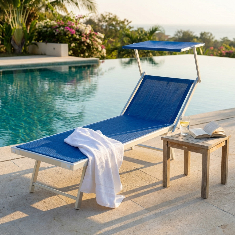 Lettino prendisole Jesolo in alluminio con seduta blu melange e parasole, posizionato a bordo piscina in un lussuoso giardino tropicale.