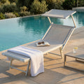 Lettino prendisole Jesolo in alluminio grigio posizionato a bordo piscina con un asciugamano bianco e un libro aperto.