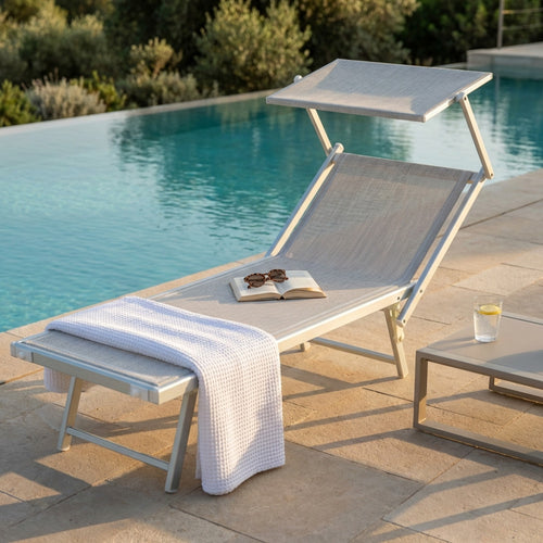 Lettino prendisole Jesolo in alluminio grigio posizionato a bordo piscina con un asciugamano bianco e un libro aperto.