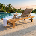Lettino prendisole Karachi in teak marrone chiaro a bordo piscina, allestito con telo bianco e tavolino laterale.