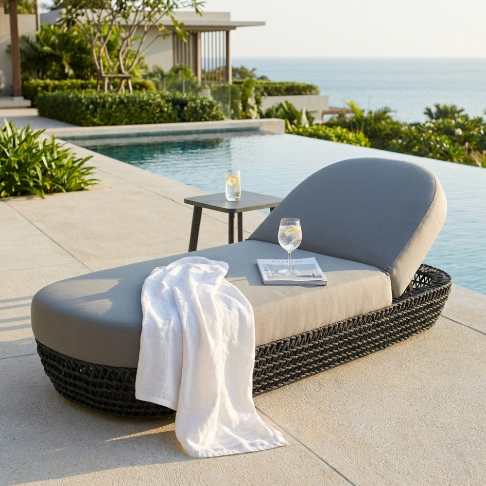 Lettino outdoor Lafayette in corda intrecciata e alluminio con vista mare e bicchiere d'acqua.