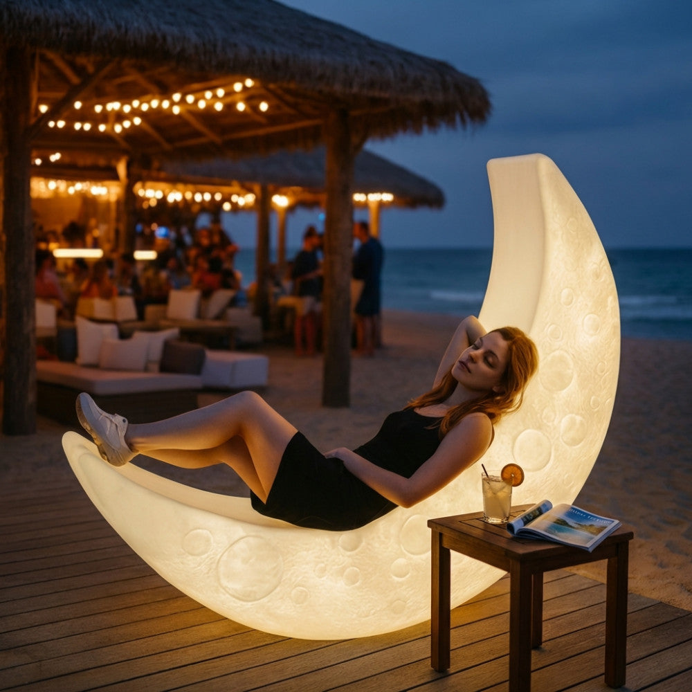 Donna che si rilassa su un lettino luminoso a forma di luna in polietilene bianco, posizionato su una spiaggia di notte.