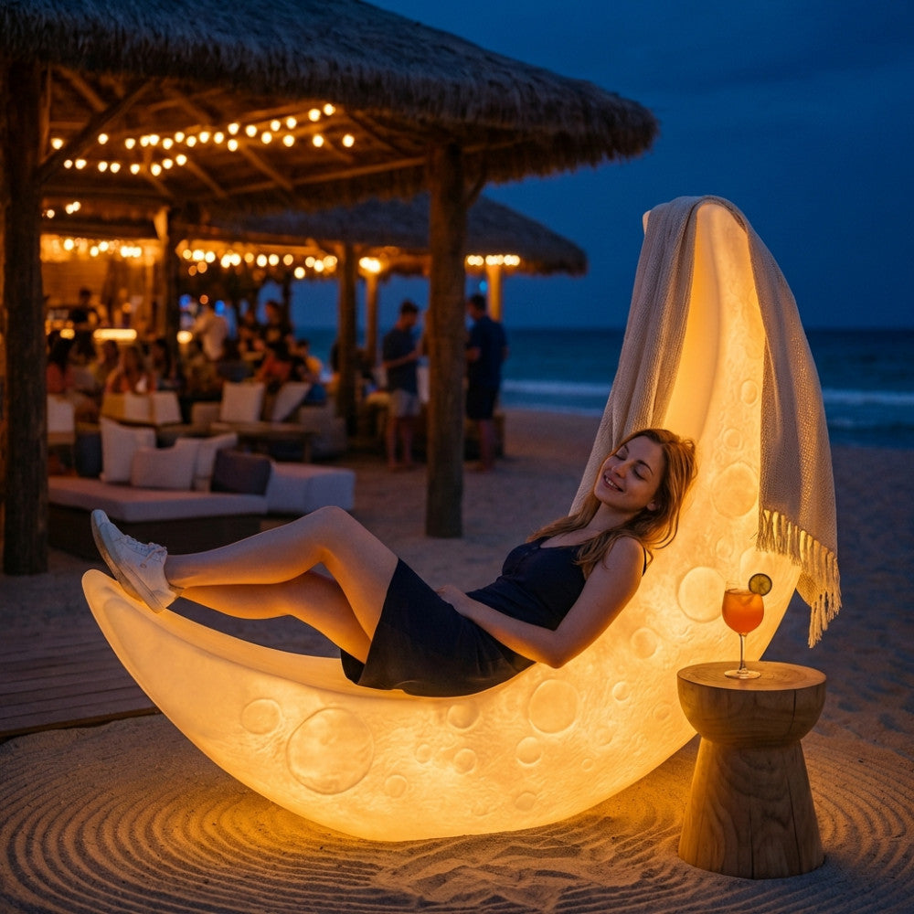 Lettino luminoso Moon acceso sulla spiaggia, con una donna distesa e una coperta drappeggiata sulla struttura scultorea.