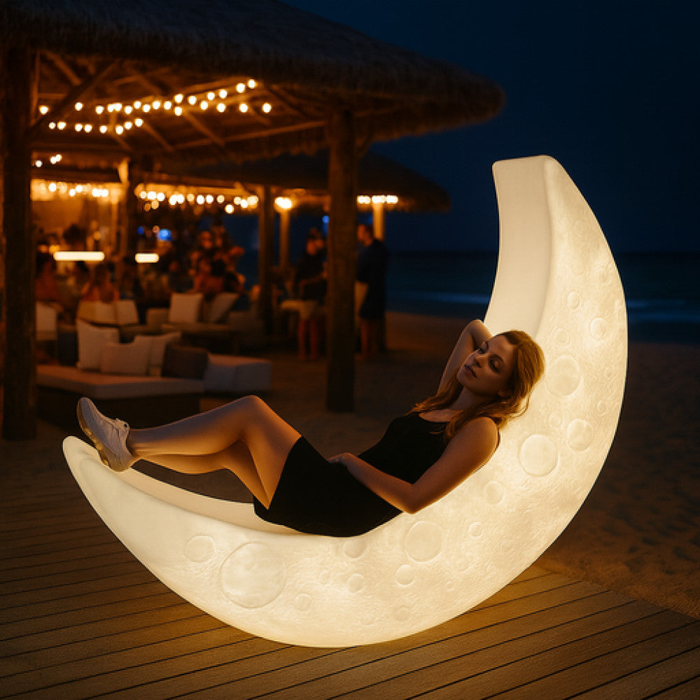 Atmosfera serale in spiaggia con il lettino luminoso a mezzaluna che diffonde una luce calda, offrendo relax ergonomico.