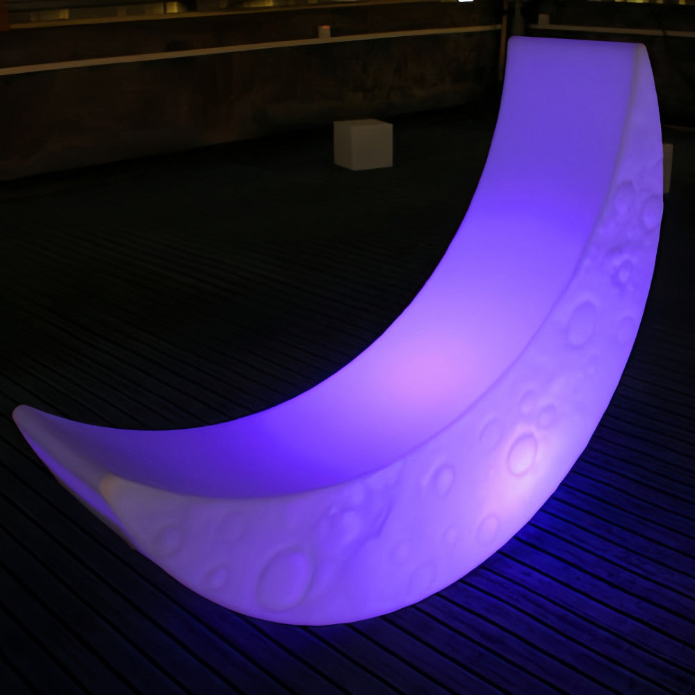 Lettino luminoso a forma di luna che emette una vibrante luce viola, posizionato su una pavimentazione in legno scuro.