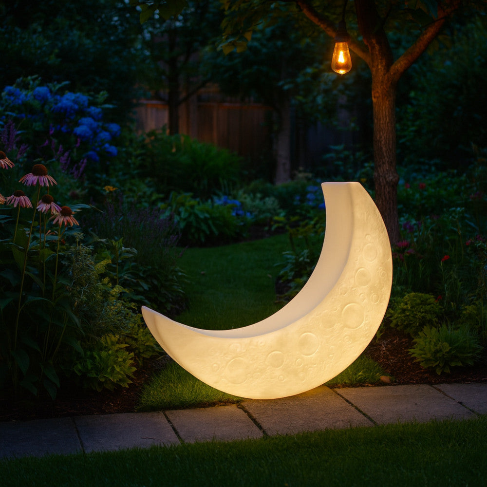 Il lettino luminoso Moon integrato in un giardino lussureggiante al crepuscolo, diffondendo un bagliore caldo tra la vegetazione.