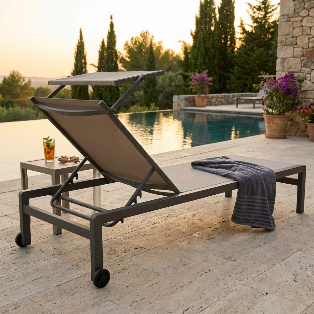 Lettino prendisole Madison in alluminio taupe posizionato a bordo di una piscina a sfioro al tramonto.