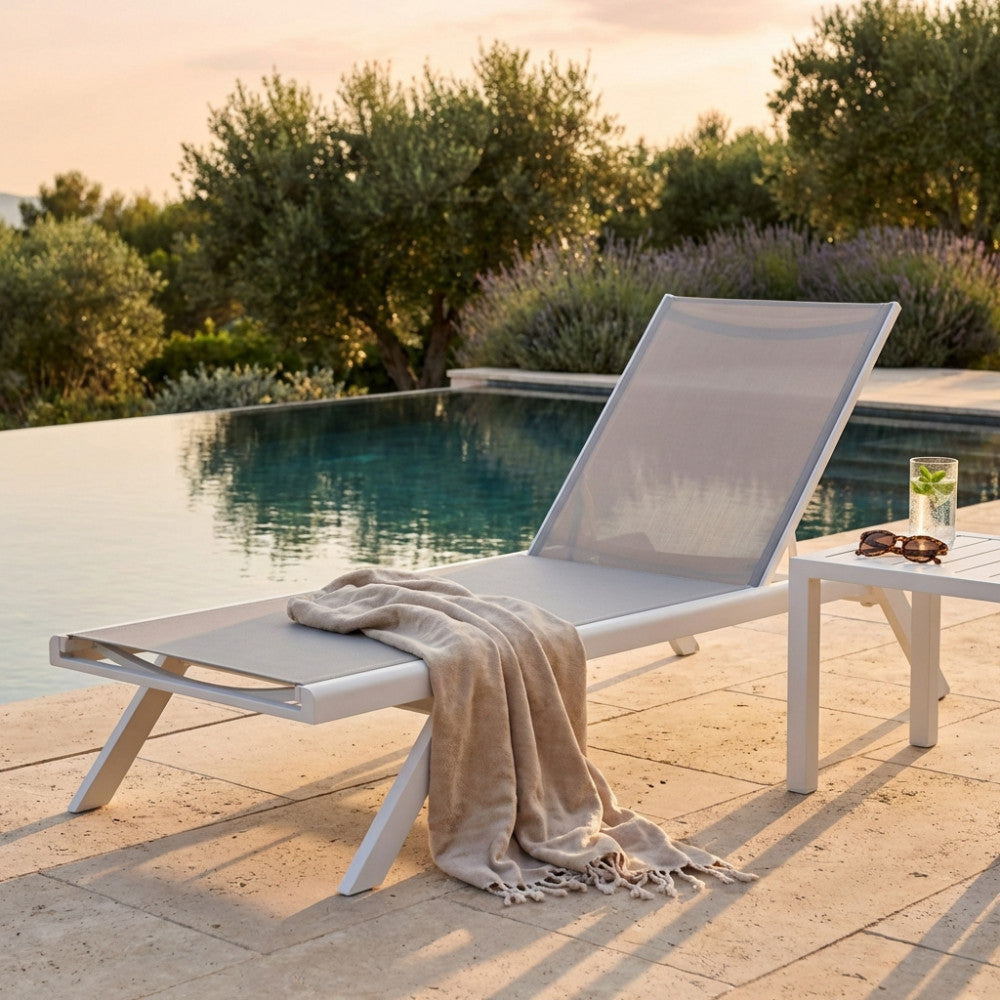 Lettino prendisole Nottingham in textilene grigio chiaro a bordo piscina al tramonto.