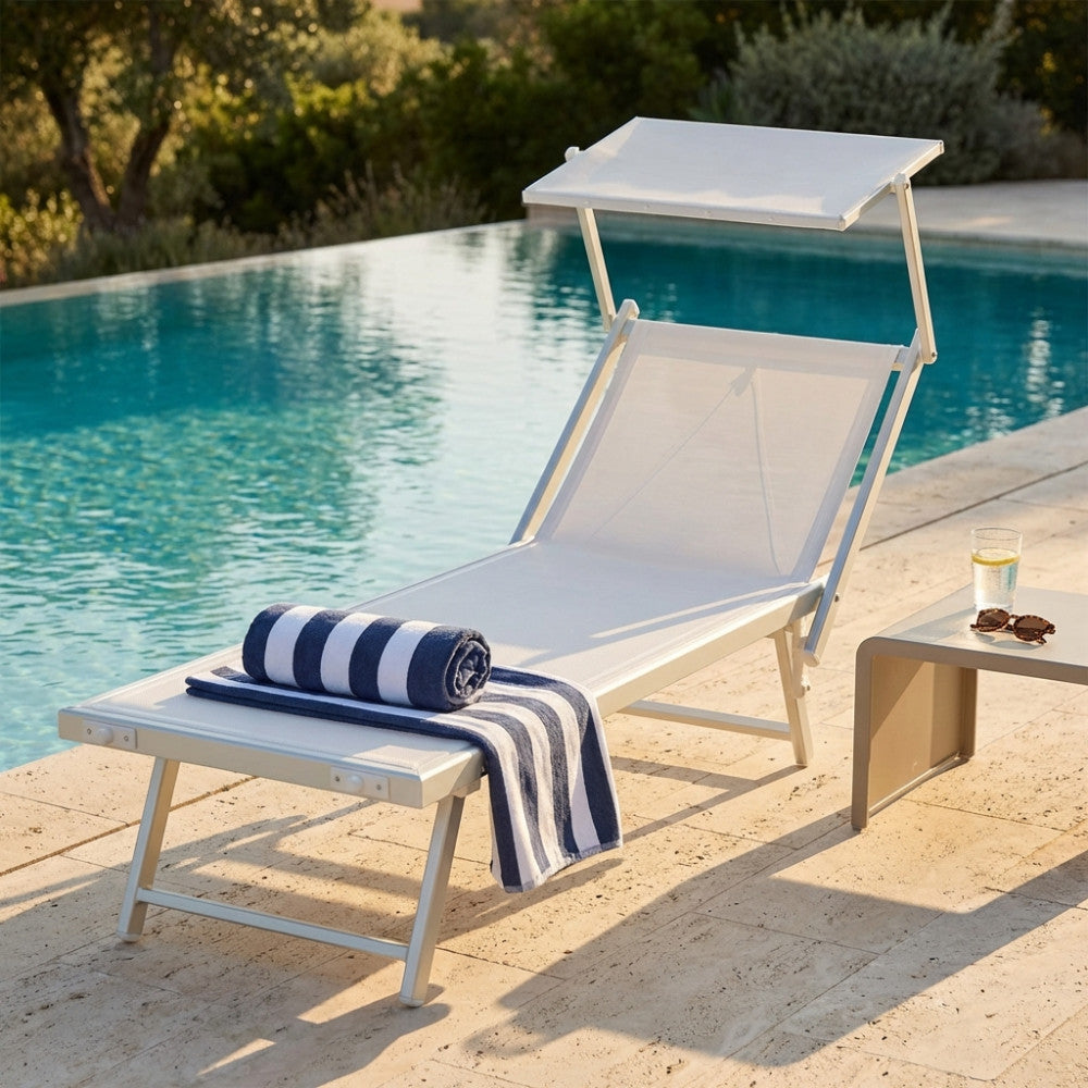 Lettino prendisole Otranto in alluminio e textilene bianco a bordo piscina con asciugamano a righe.