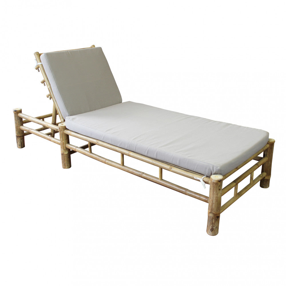 Lettino prendisole Blue Lagoon in bamboo di colore marrone con cuscino, posizionato in un giardino lussureggiante.