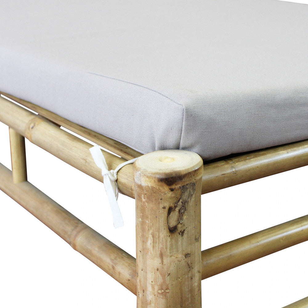 Lettino prendisole Blue Lagoon in bamboo di colore marrone con cuscino, posizionato in un giardino lussureggiante.