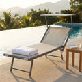 Lettino prendisole Rimini in alluminio grigio e textilene beige posizionato a bordo piscina con asciugamano bianco e tavolino in teak.