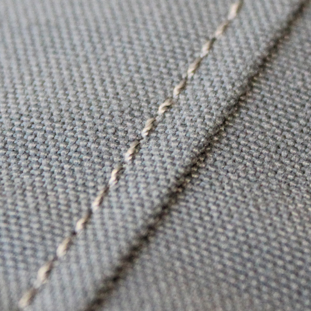 Macro sulle cuciture sartoriali e la trama materica del rivestimento grigio.