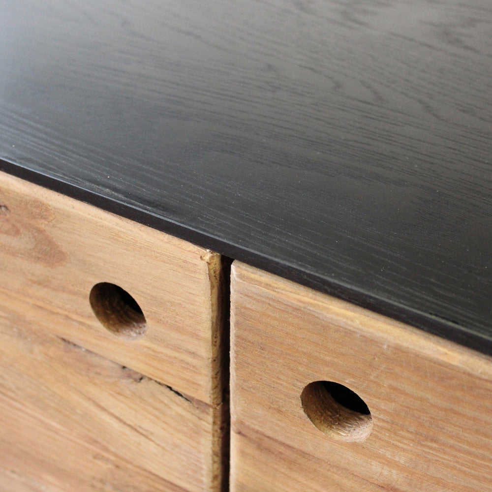 Dettaglio ravvicinato del ripiano in metallo nero e del bordo in legno rustico della credenza ANSELM.