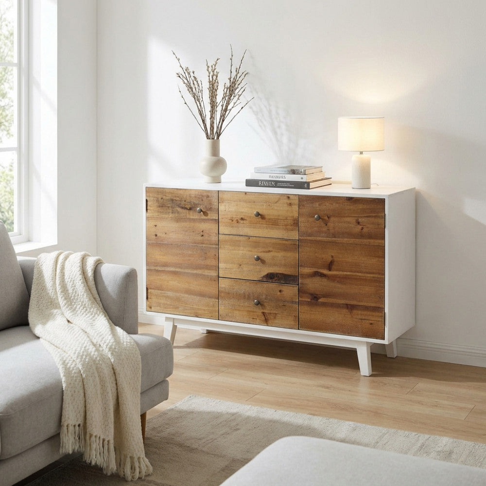Credenza Austen in legno bianco e marrone ambientata in un salotto luminoso con divano grigio e lampada da tavolo.
