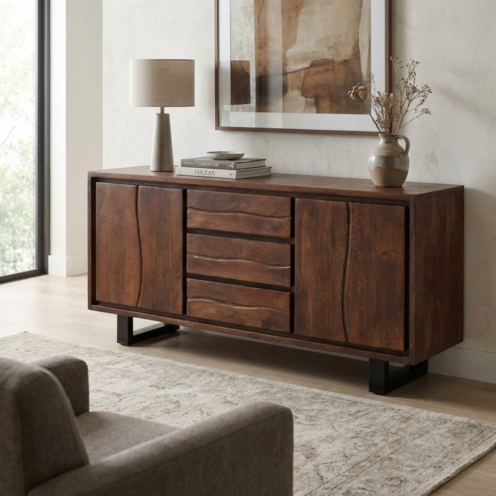 Vista frontale della credenza Brennan in legno di acacia in un soggiorno luminoso, allestita con una lampada in ceramica e fiori secchi.