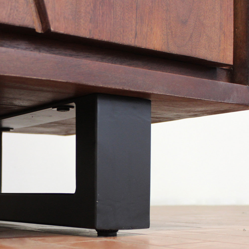 Primo piano della robusta base in metallo nero e del bordo inferiore liscio del mobile in legno di acacia.
