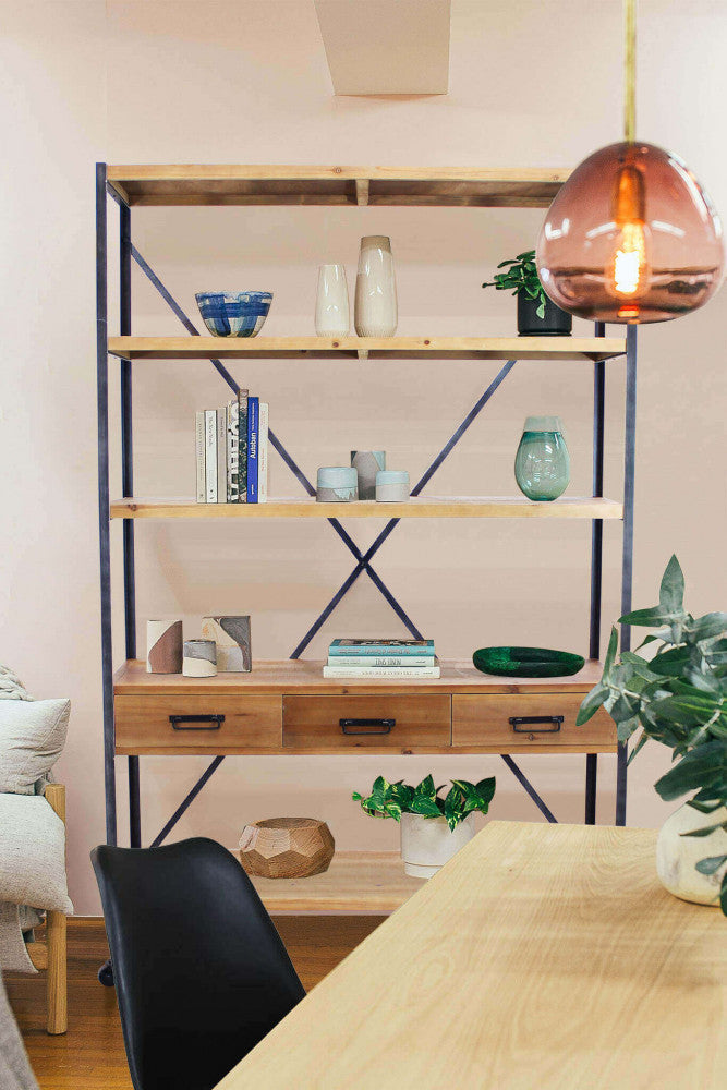 Libreria Buck elegantemente allestita con vasi in ceramica e libri, vista attraverso un tavolo da pranzo in legno con lampada a sospensione ambrata.