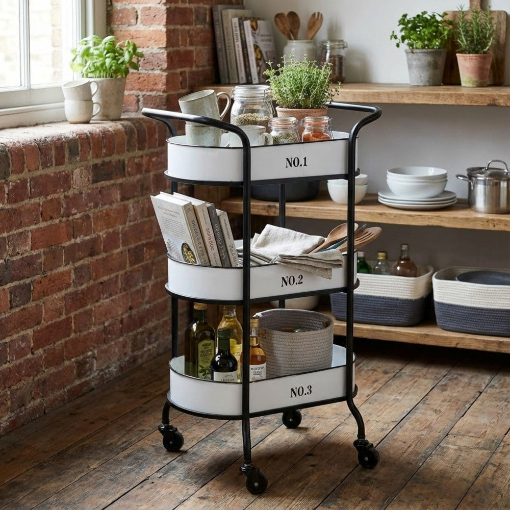 Carrello in acciaio inserito in un contesto rustico con mattoni a vista, allestito con bottiglie e libri di cucina.