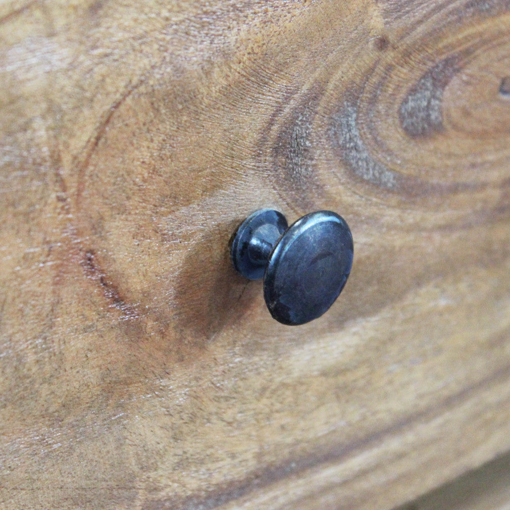 Dettaglio macro del pomello metallico scuro su un cassetto, che contrasta con la superficie marrone materica.
