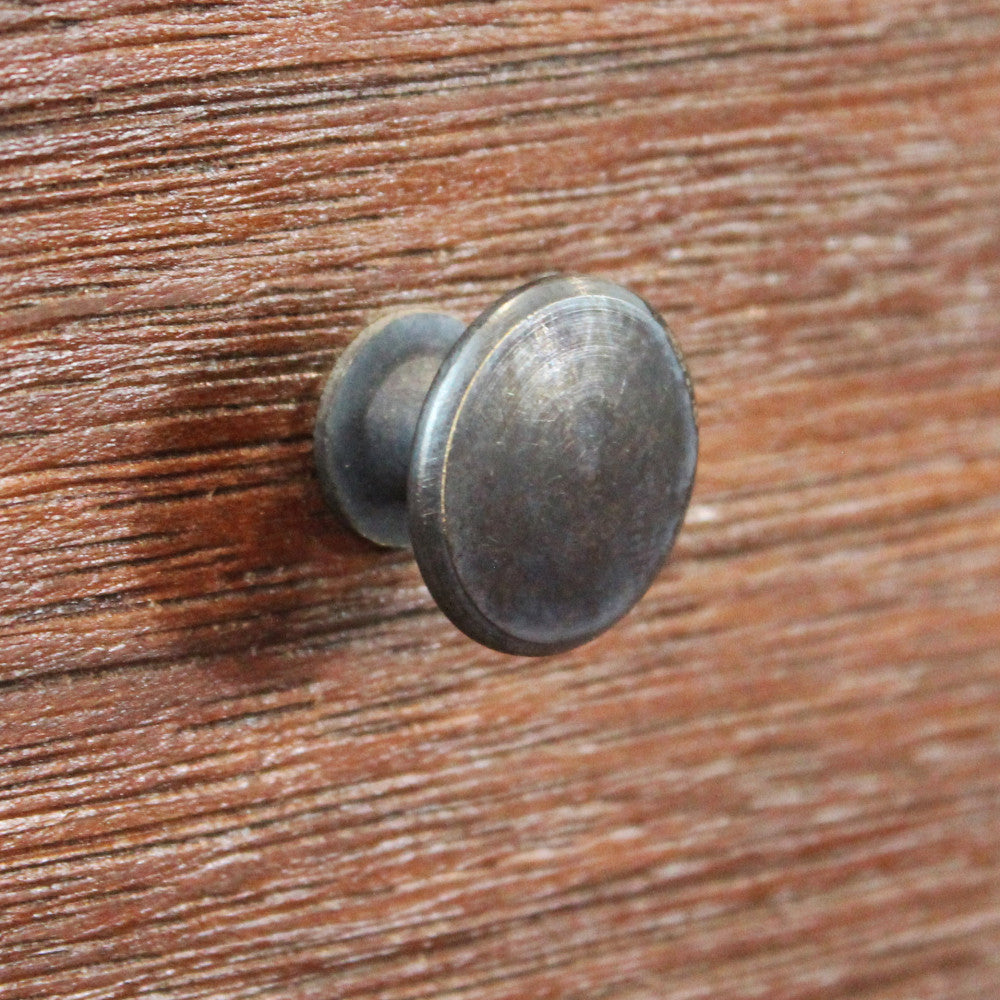 Primo piano estremo della maniglia rotonda in metallo anticato e della texture ruvida del frontale del cassetto.