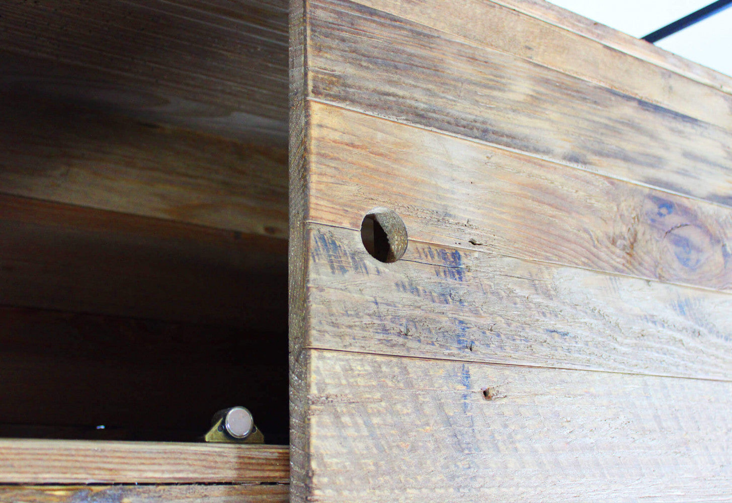 Primo piano della superficie in pino riciclato, che rivela i dettagli tattili delle venature, le imperfezioni naturali e la maniglia circolare minimalista.