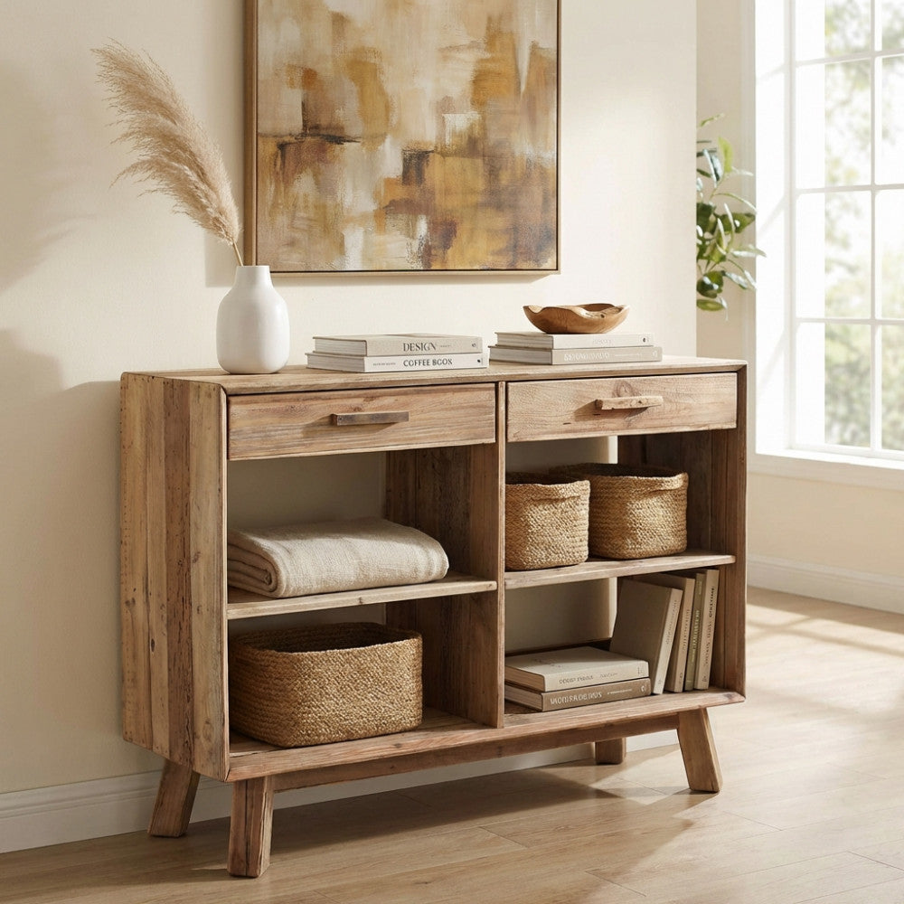 Dettaglio laterale della credenza vintage in legno massello, decorata con libri d'arte, coperte neutre e un vaso in ceramica bianca.