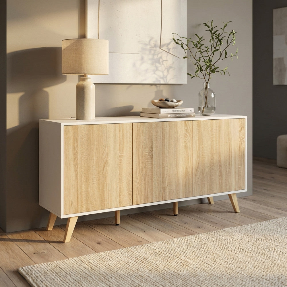 Credenza Elton in truciolare bilaminato bianco e naturale, ambientata in un soggiorno luminoso con lampada e vaso decorativo.