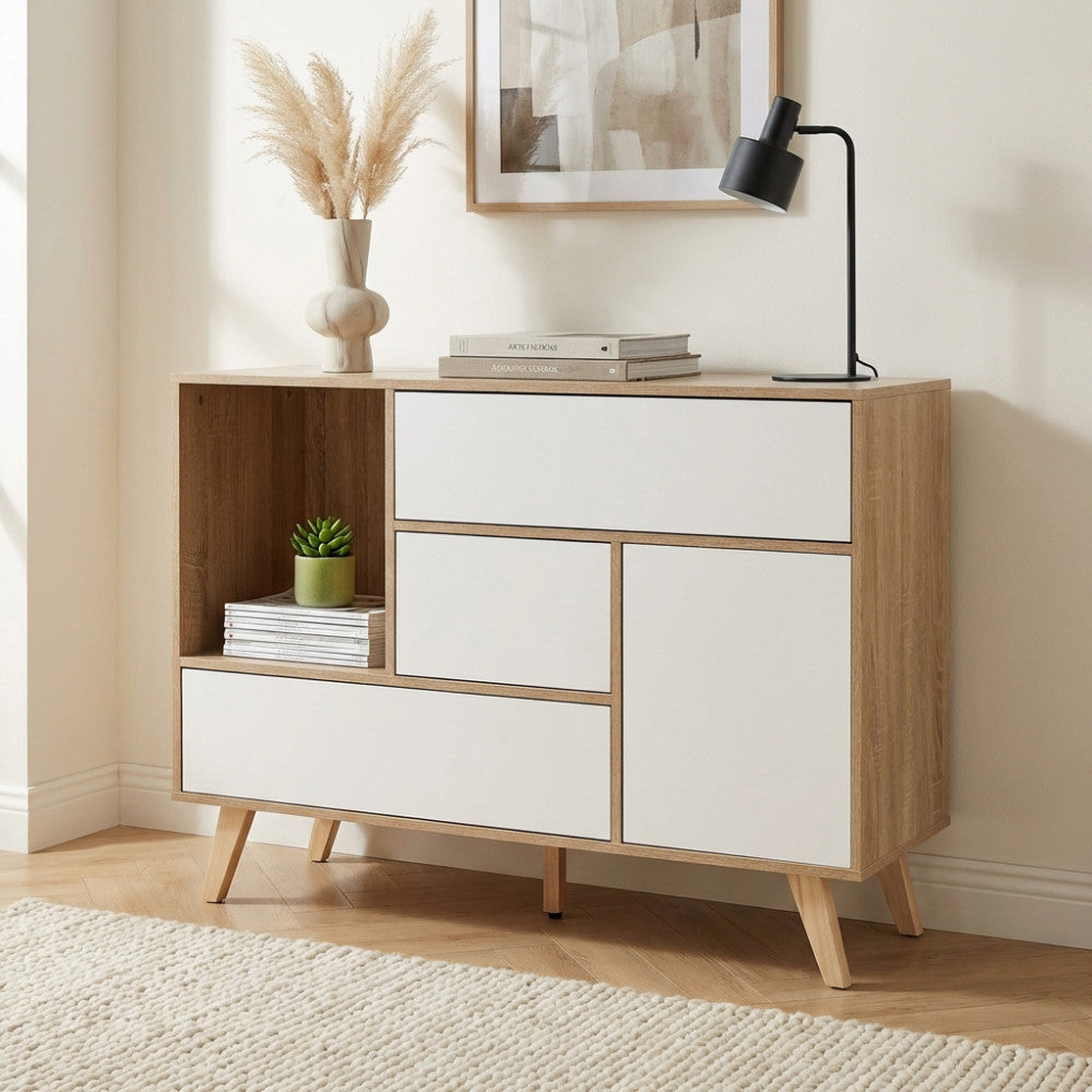 Credenza Emory in truciolare bilaminato bianco e naturale, ambientata in un soggiorno moderno con lampada da tavolo e vaso decorativo.