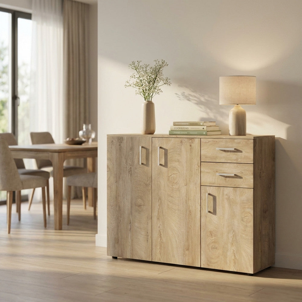 Vista angolare della credenza in truciolare bilaminato rovere chiaro con vaso di fiori e lampada da tavolo.