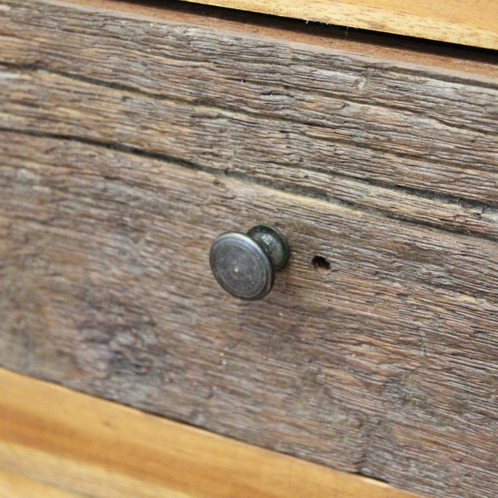Dettaglio del pomello in metallo scuro sul cassetto in legno grezzo di recupero.