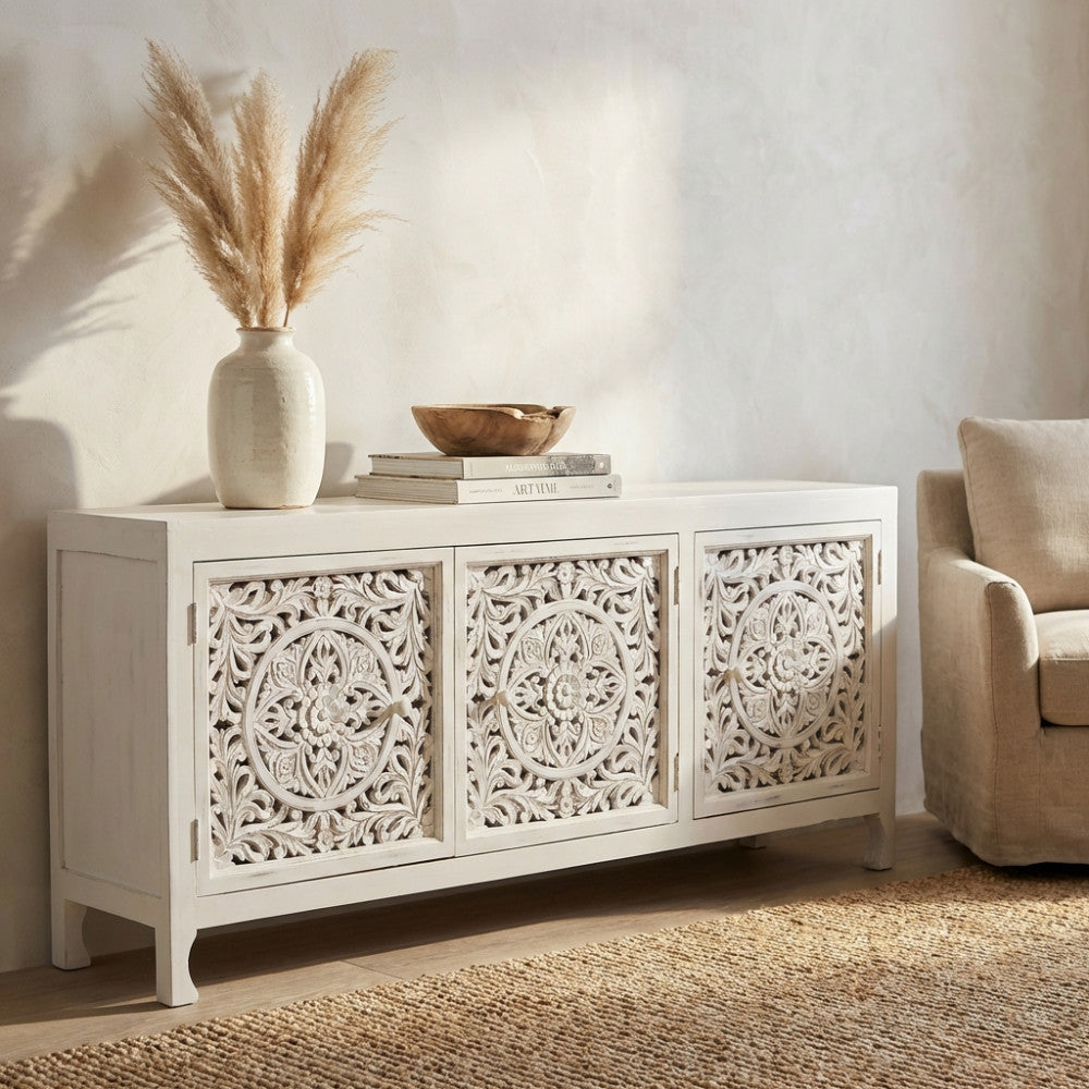 Vista frontale ambientata della credenza boho chic bianca, caratterizzata da intricati intagli floreali e accenti in legno naturale.