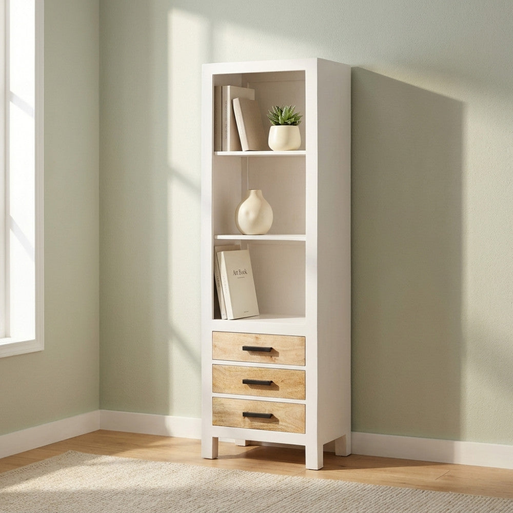 Libreria Jeffrey in legno di mango bianco con tre cassetti, ambientata in un angolo luminoso con libri e una pianta.