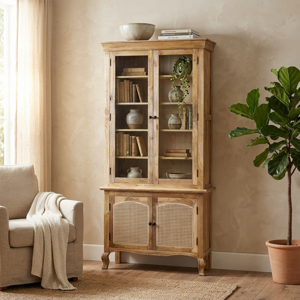 Vetrina Kaleb in legno di mango con ante in vetro e dettagli in rattan, affiancata da una pianta d'appartamento.