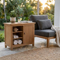Credenza Lexington 90 in teak premium allestita su un patio in pietra accanto a una poltrona moderna, con asciugamani arrotolati e una pianta in vaso.