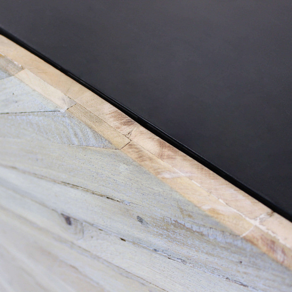 Dettaglio ravvicinato del top in metallo nero liscio che contrasta con la texture ruvida e naturale del legno di mango sulla struttura della credenza.
