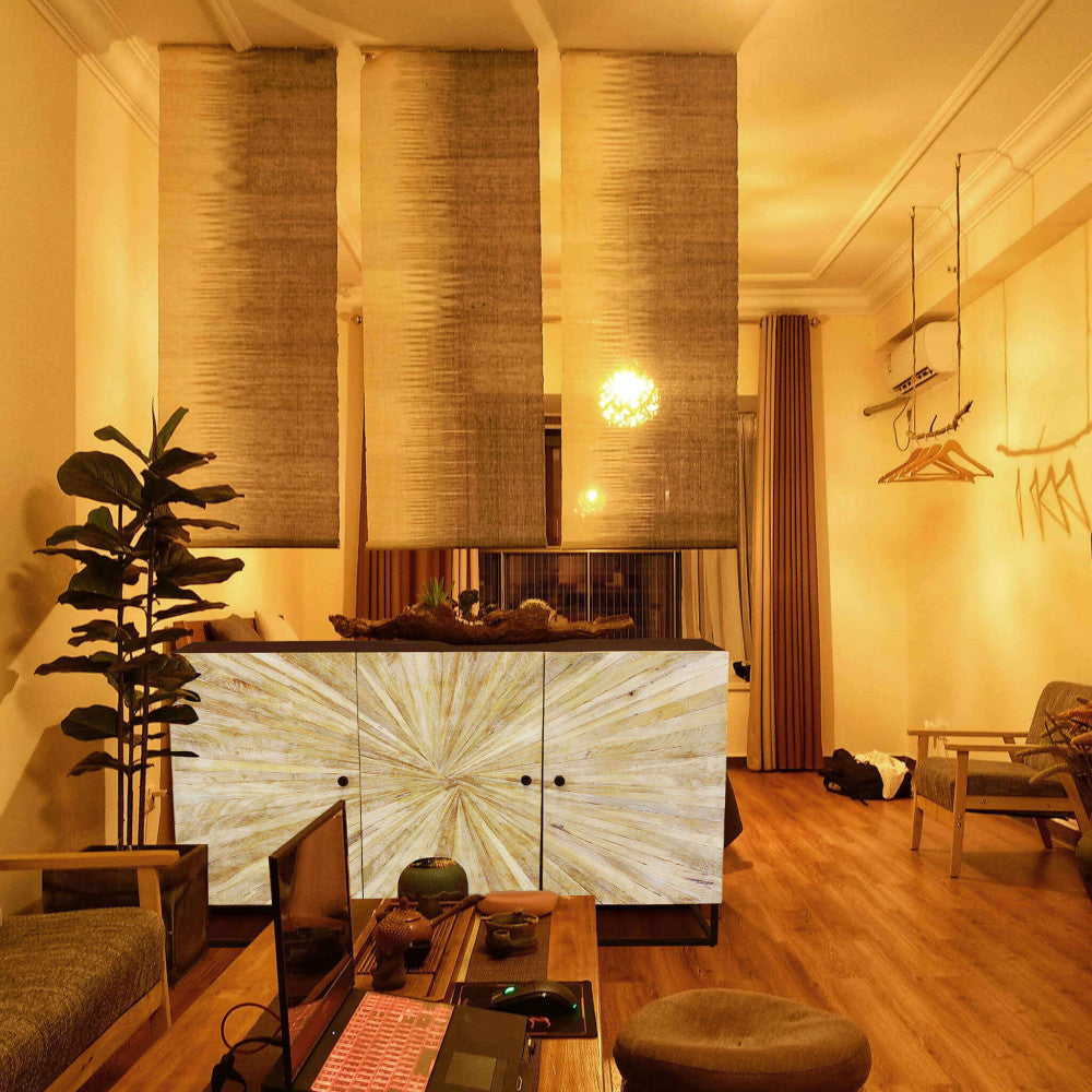 Ambientazione serale calda e accogliente con la credenza Spencer illuminata da luci soffuse, integrata in un salotto dal design etnico e contemporaneo.