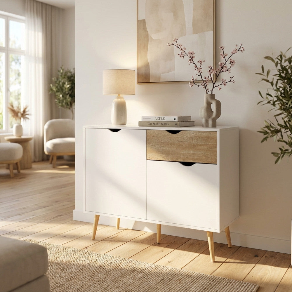 Credenza THEODORE in legno bianco e marrone ambientata in un luminoso soggiorno moderno con lampada in ceramica e rami decorativi.