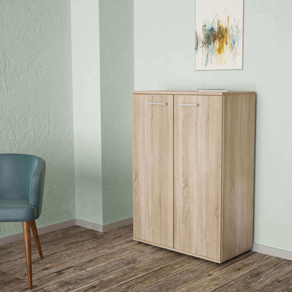 Mobiletto inserito in un contesto moderno con pareti verde salvia, pavimento in legno scuro e una sedia di design.