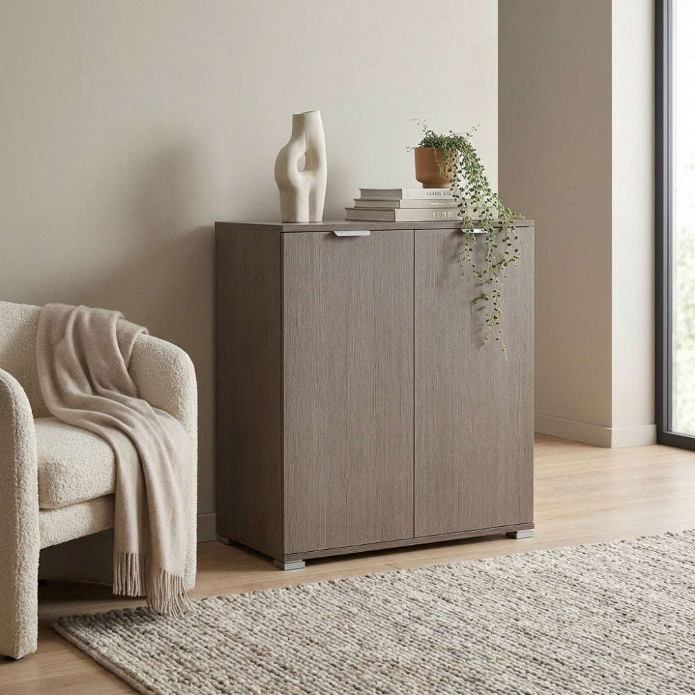 Mobiletto a due ante in rovere grigio ambientato in un soggiorno moderno accanto a una poltrona in bouclé.