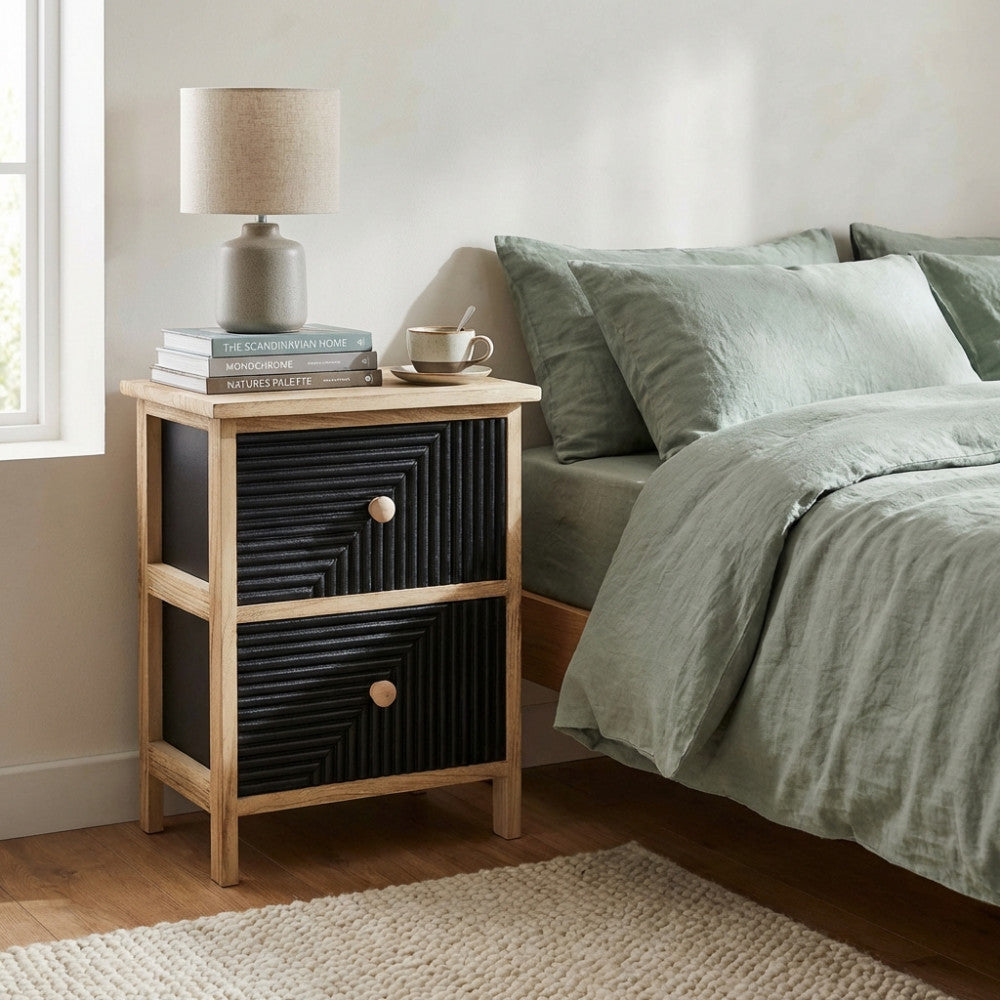 Comodino Anton dal design industrial affiancato a un letto con lenzuola verde salvia.