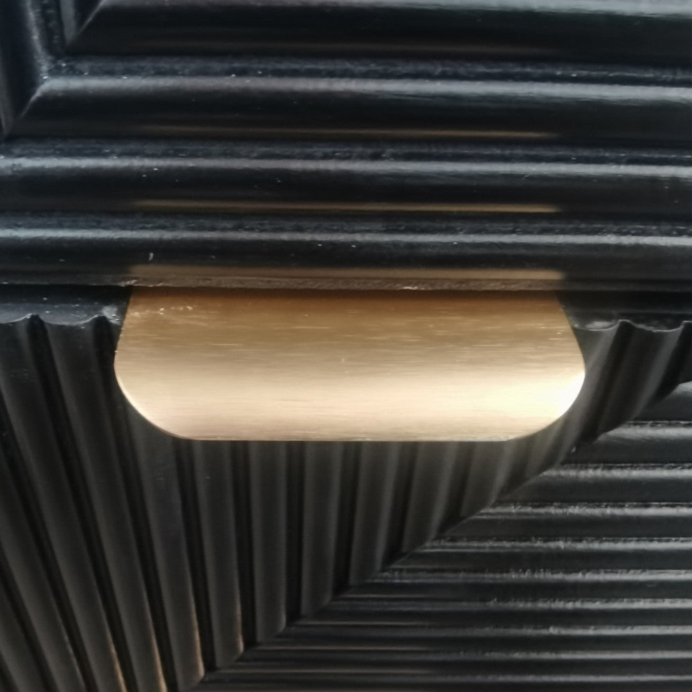 Macro fotografia della maniglia dorata del comodino ASIER, che esalta il contrasto materico con il legno nero lavorato.