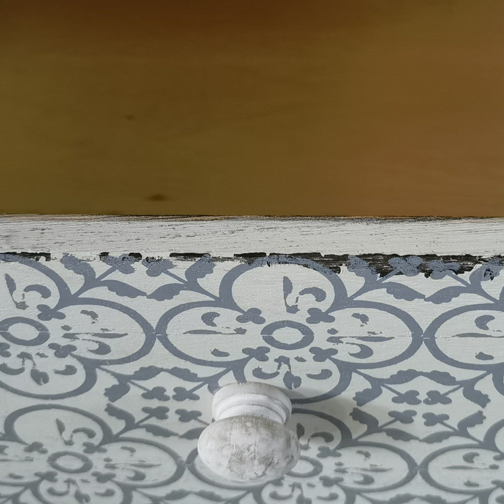 Dettaglio ravvicinato del cassetto con motivo floreale grigio e bianco e pomello in legno anticato.