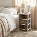 Comodino vintage Alonso in legno bianco posizionato accanto a un letto matrimoniale con lenzuola in lino.