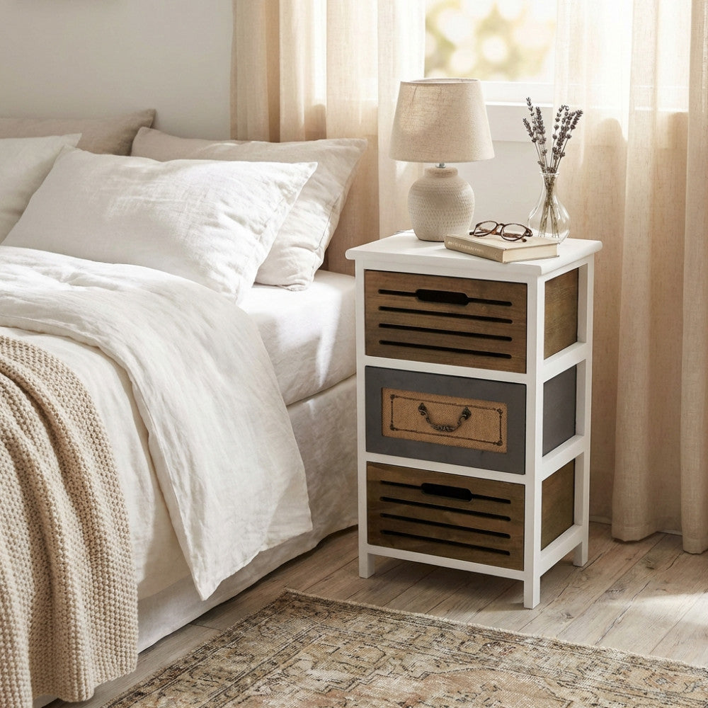 Comodino vintage Alonso in legno bianco posizionato accanto a un letto matrimoniale con lenzuola in lino.