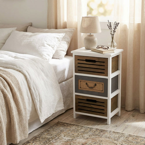 Comodino vintage Alonso in legno bianco posizionato accanto a un letto matrimoniale con lenzuola in lino.